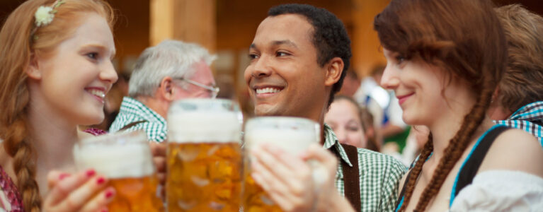 Three persons holding beer mugs and smiling during Oktoberfest