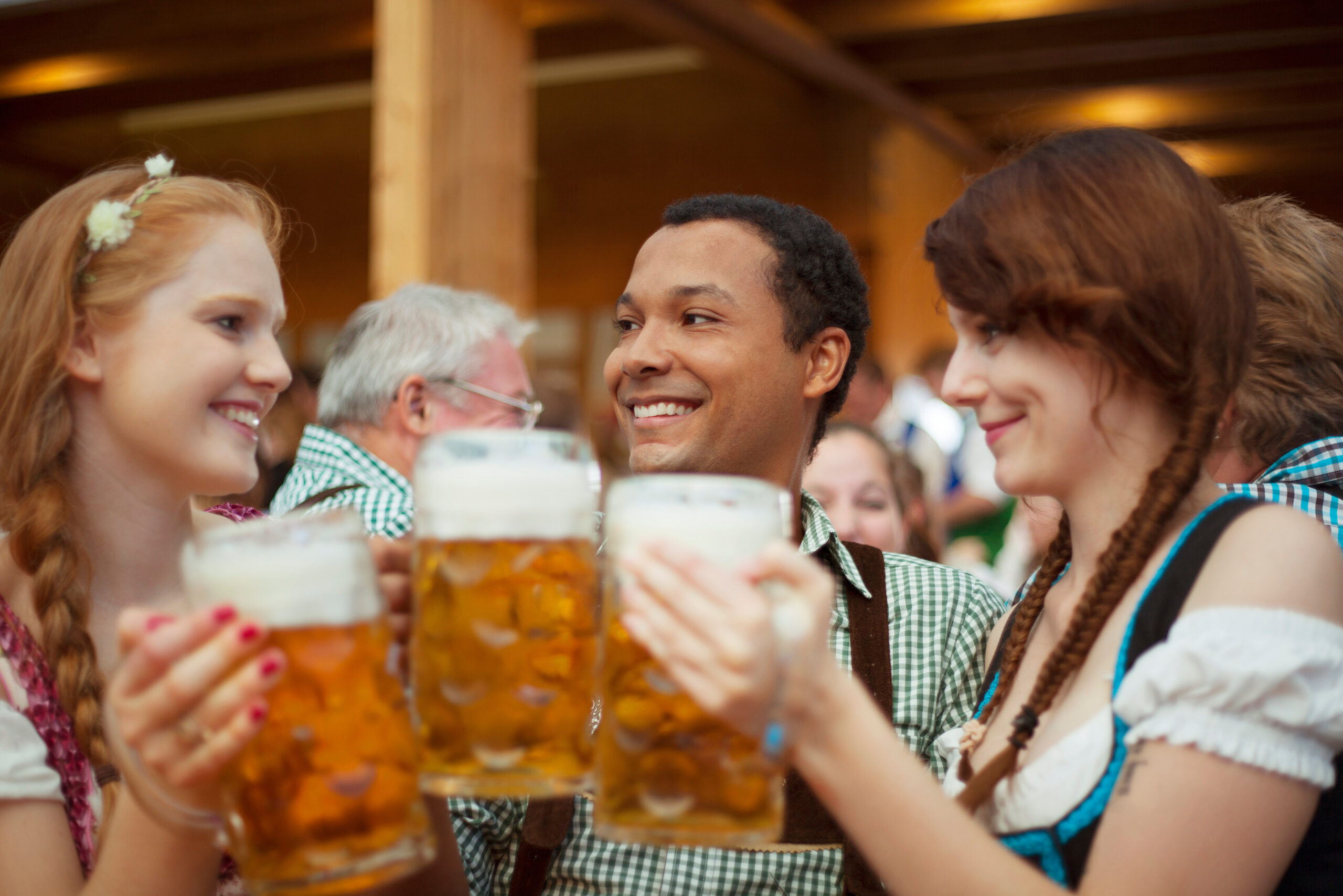 Three persons holding beer mugs and smiling during Oktoberfest